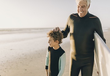 Un homme et son petit fils marchent en bord de mer après avoir surfé.